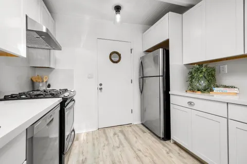 a kitchen with stainless steel appliances a refrigerator a stove a sink and white cabinets with wooden floor