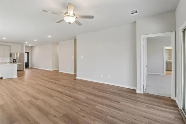a view of an empty room with wooden floor a ceiling fan and kitchen view