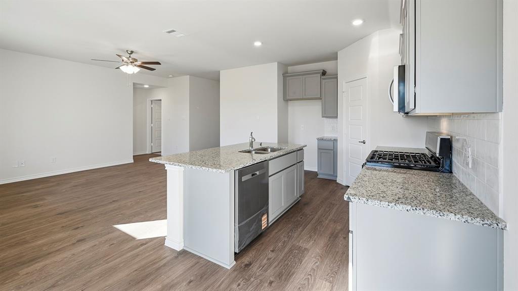419 Epiphany Lane Lavon, TX 75166 - Photo 10 of 31 Modern kitchen featuring light gray cabinetry, a gas range, a built-in microwave, and an island with an undermount sink and integrated dishwasher