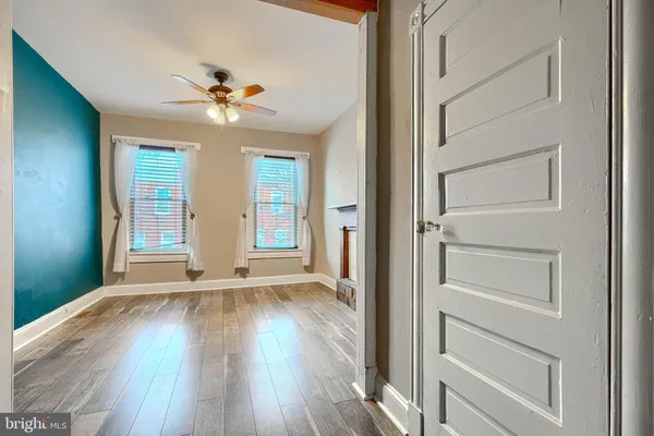 a view of an empty room with wooden floor and a ceiling fan