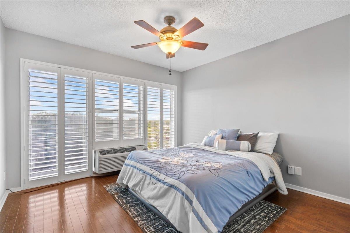 Bedroom with ceiling fan, a textured ceiling, wood finished floors, a wall mounted air conditioner, and baseboards