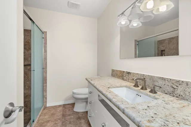 a bathroom with a granite countertop sink a toilet and a mirror