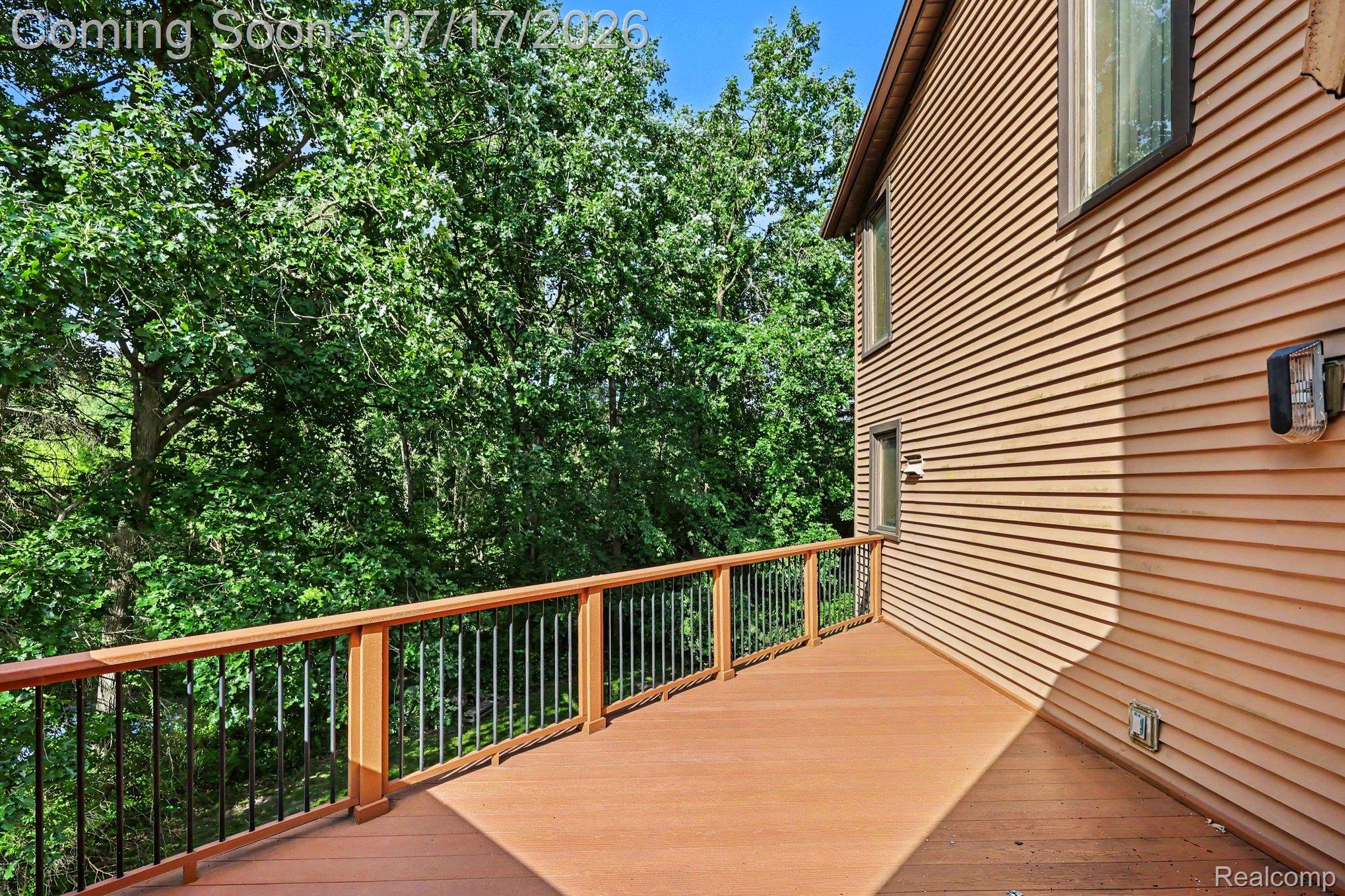 5685 Paint Valley Drive Rochester, MI 48306 - Photo 43 of 66 Expansive exterior deck featuring a composite wood-finish surface, wood railing with black metal balusters, and a beige horizontal siding facade