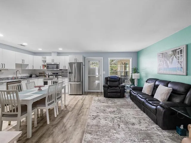 a kitchen with stainless steel appliances granite countertop a stove top oven a sink dishwasher a refrigerator and white cabinets with wooden floor