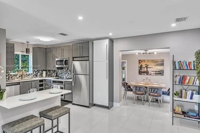 a kitchen with stainless steel appliances a refrigerator a sink a stove a dining table and chairs