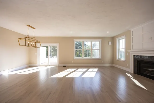 a view of an empty room with wooden floor fireplace and a window