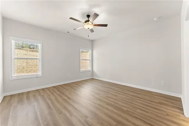 an empty room with wooden floor fan and windows