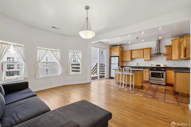 a living room with stainless steel appliances furniture wooden floor and a kitchen