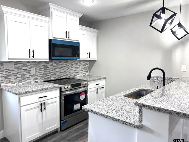 a kitchen with granite countertop a sink stainless steel appliances and white cabinets