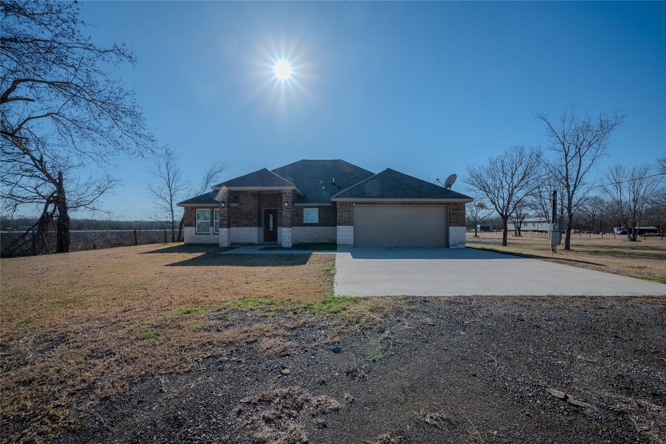 A beautiful brick facade greets you at the end of a wide driveway, perfectly situated amidst the picturesque property landscape.