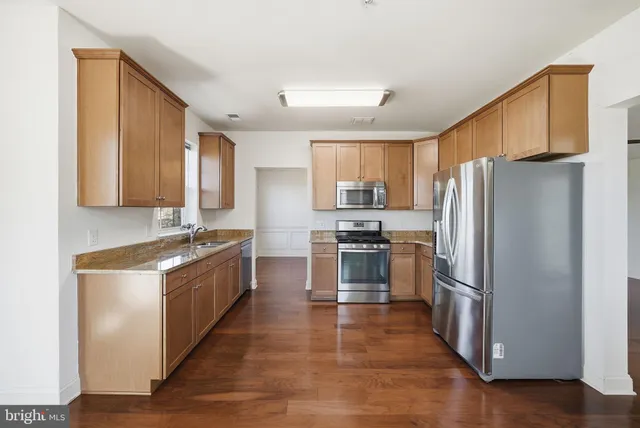 a kitchen with granite countertop stainless steel appliances a refrigerator cabinets and wooden floor