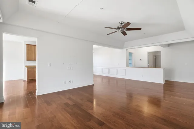 an empty room with wooden floor a ceiling fan and windows