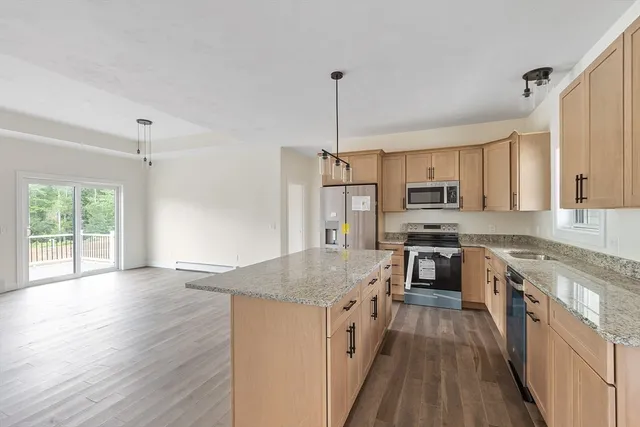 a kitchen with stainless steel appliances granite countertop a stove top oven a sink dishwasher a refrigerator and a dining table with wooden floor