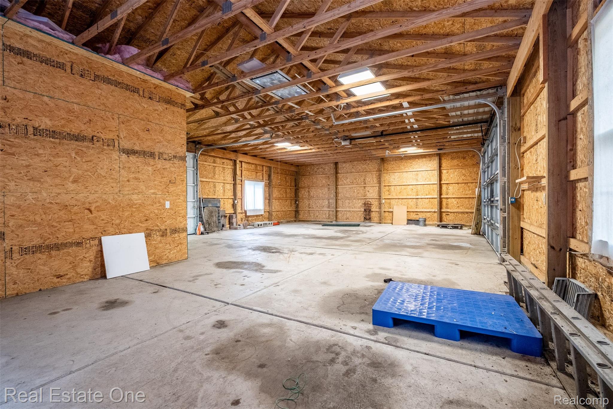 11030 Marshall Road South Lyon, MI 48178 - Photo 68 of 83 Expansive interior space featuring exposed wood trusses, multiple skylights, concrete flooring, and a large roll-up door