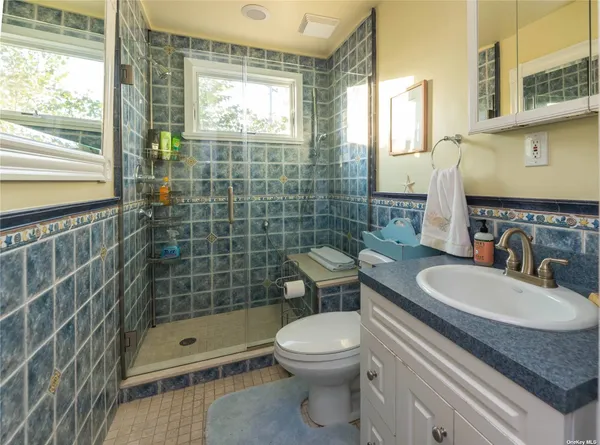 a bathroom with a granite countertop sink a toilet a mirror and shower