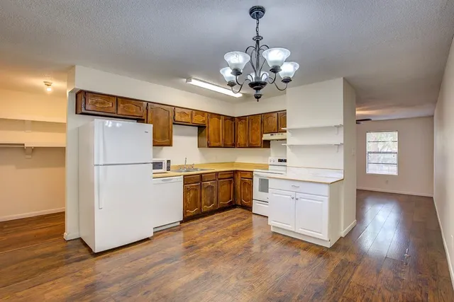 a kitchen with stainless steel appliances granite countertop a refrigerator a sink dishwasher a stove and white cabinets with wooden floor