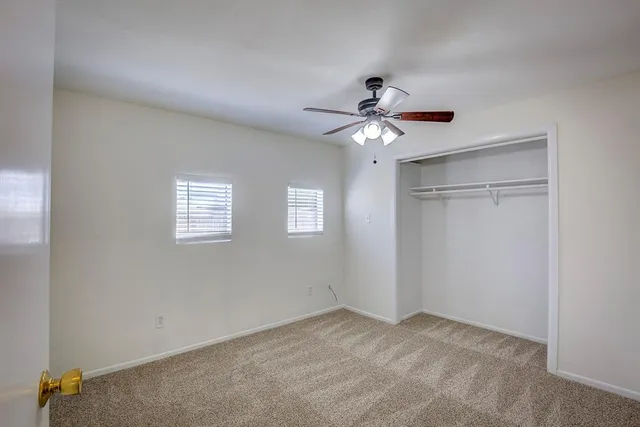 an empty room with a chandelier fan and windows