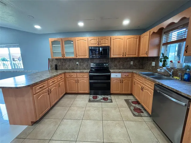 a large kitchen with stainless steel appliances granite countertop a stove top oven a sink a counter top space and cabinets