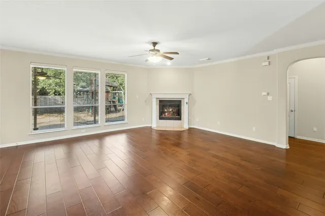 an empty room with wooden floor chandelier fan and windows