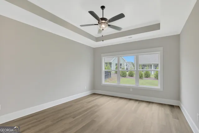 an empty room with wooden floor chandelier fan and windows