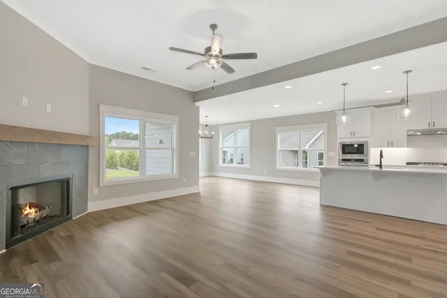 a view of an empty room and kitchen with wooden floor