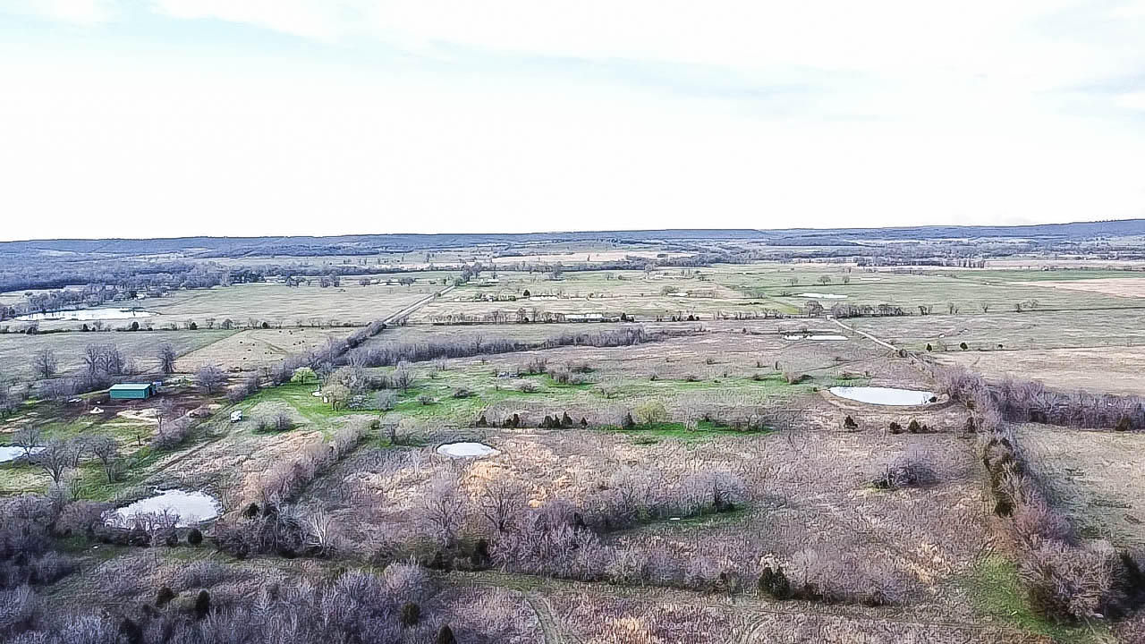 Expansive rural acreage featuring multiple ponds, scattered trees, and a distant building