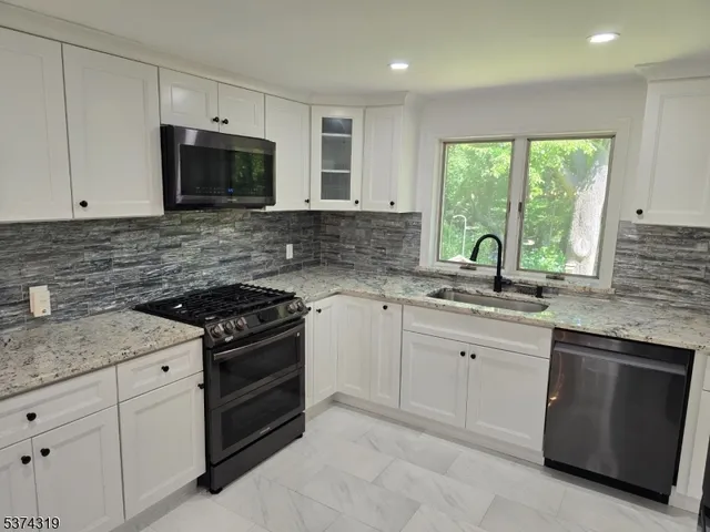 a kitchen with granite countertop white cabinets stainless steel appliances a sink and a window