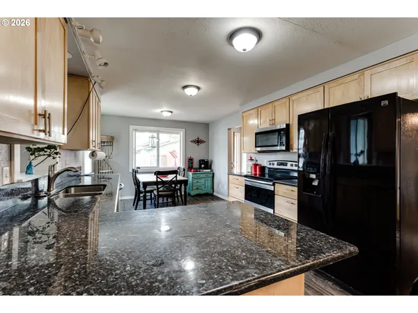 a kitchen view with stainless steel appliances granite countertop a refrigerator stove top oven dining table and chairs