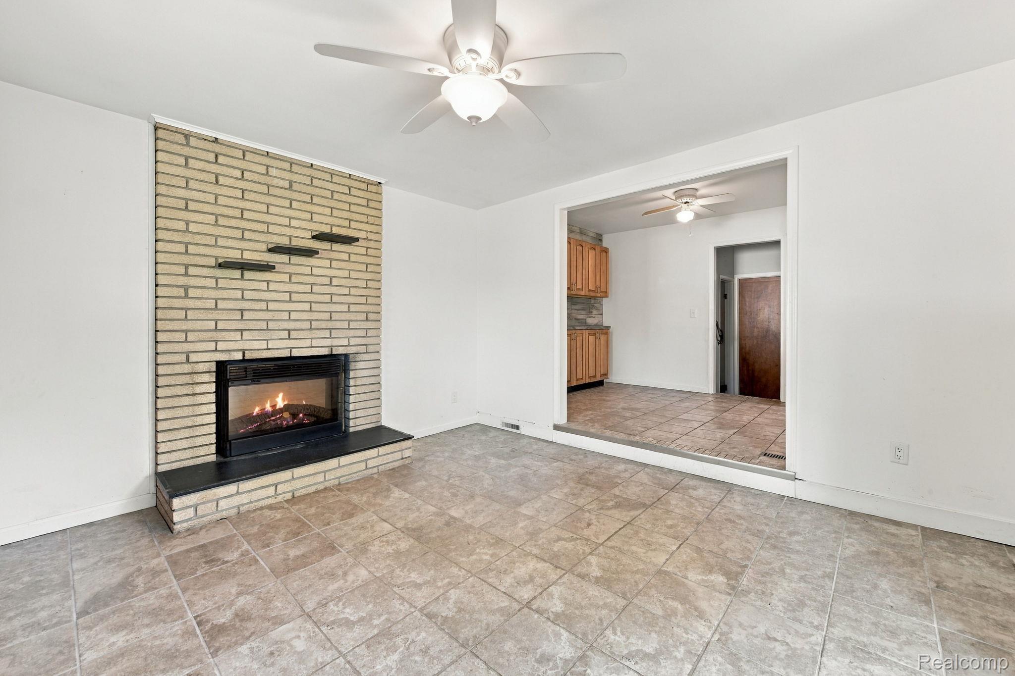 13265 12 Mile Road Warren, MI 48088 - Photo 23 of 33 Brick fireplace with a black hearth, ceiling fan, and tiled flooring