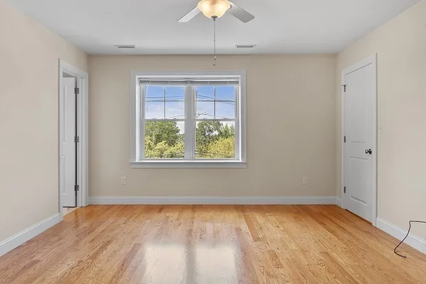 a view of an empty room with wooden floor and a ceiling fan