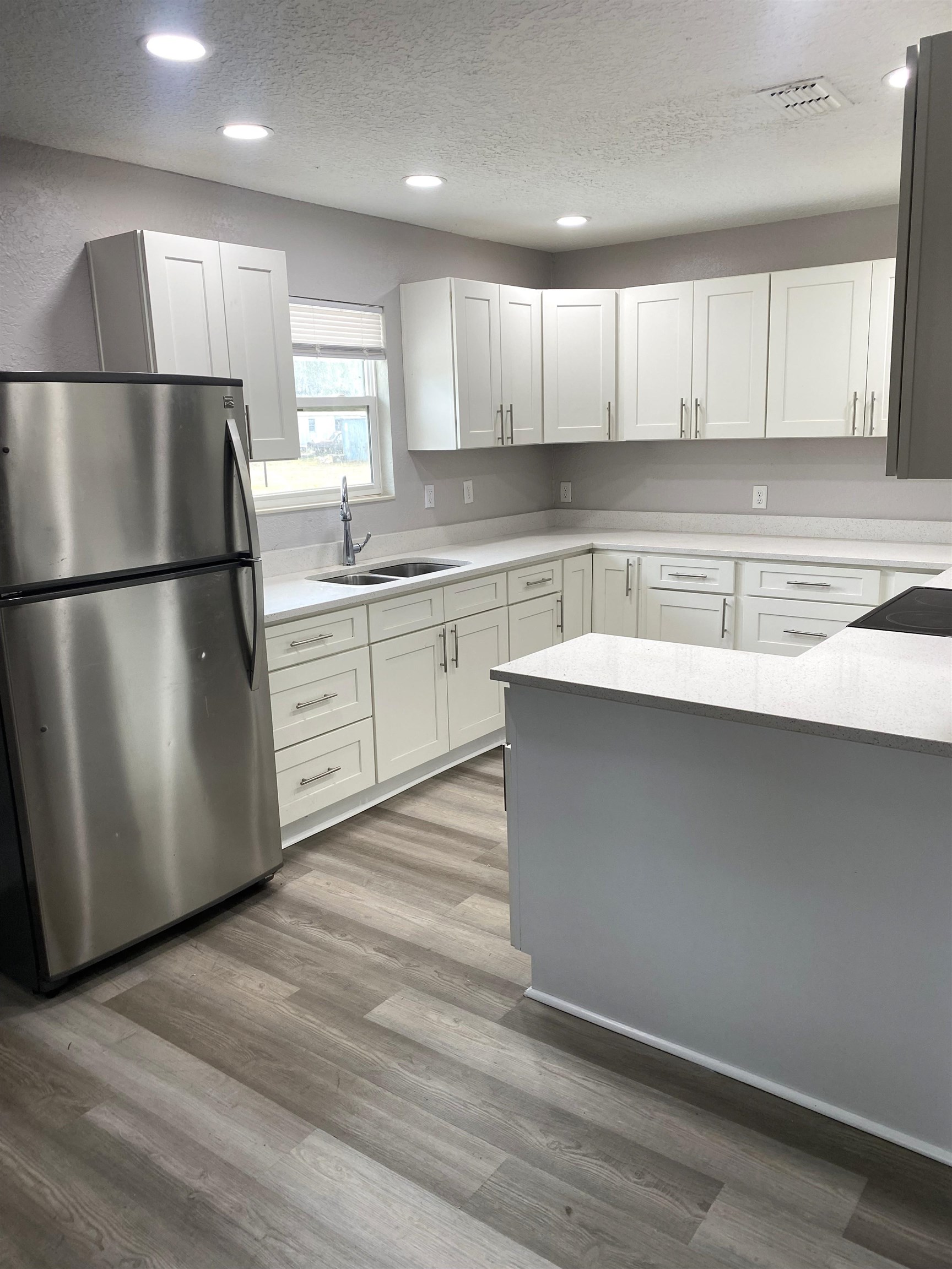 Kitchen featuring freestanding refrigerator, a textured ceiling, recessed lighting, light stone counters, and white cabinetry