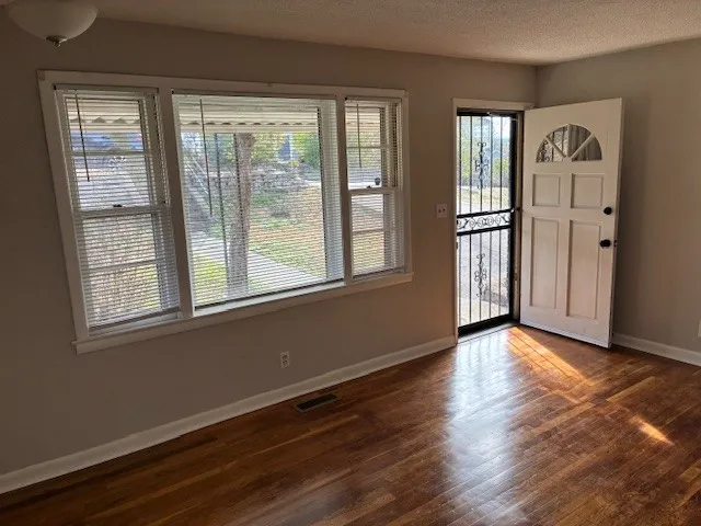 a view of an empty room with wooden floor and a window