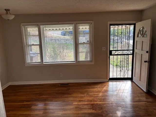 a view of an empty room with wooden floor and a window