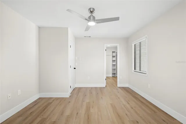 an empty room with wooden floor ceiling fan and windows