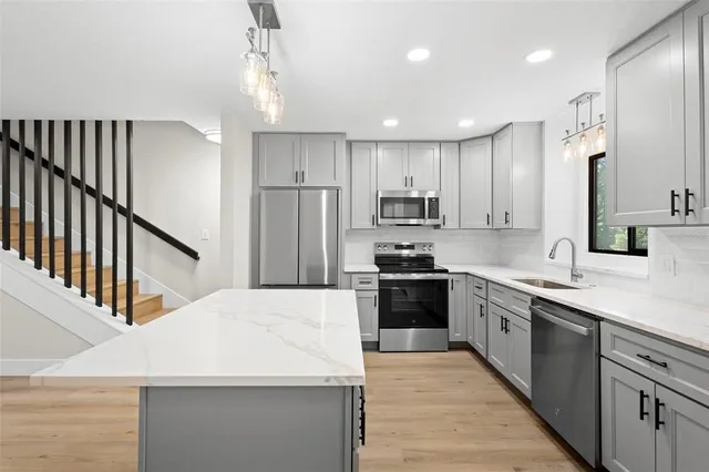 a kitchen with stainless steel appliances kitchen island granite countertop a refrigerator a sink dishwasher a stove and white cabinets with wooden floor