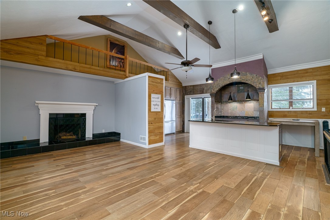 3165 East Sprague Road Independence, OH 44131 - Photo 8 of 41 livving area with fireplace, luxury vinyl flooring exposed beams, vaulted ceiling open to kitchen with island, granite counter tops, wood paneling, stone framed cooktop with pendant lighting and ceiling fan.