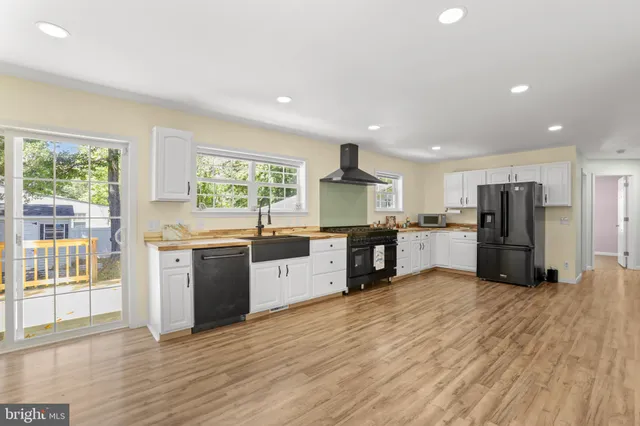 a large kitchen with stainless steel appliances granite countertop a stove a sink dishwasher a refrigerator and white cabinets with wooden floor