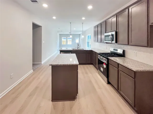 a large kitchen with stainless steel appliances kitchen island granite countertop a stove a sink dishwasher and a microwave with wooden floor