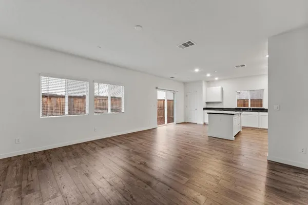 a view of an empty room with wooden floor and a kitchen