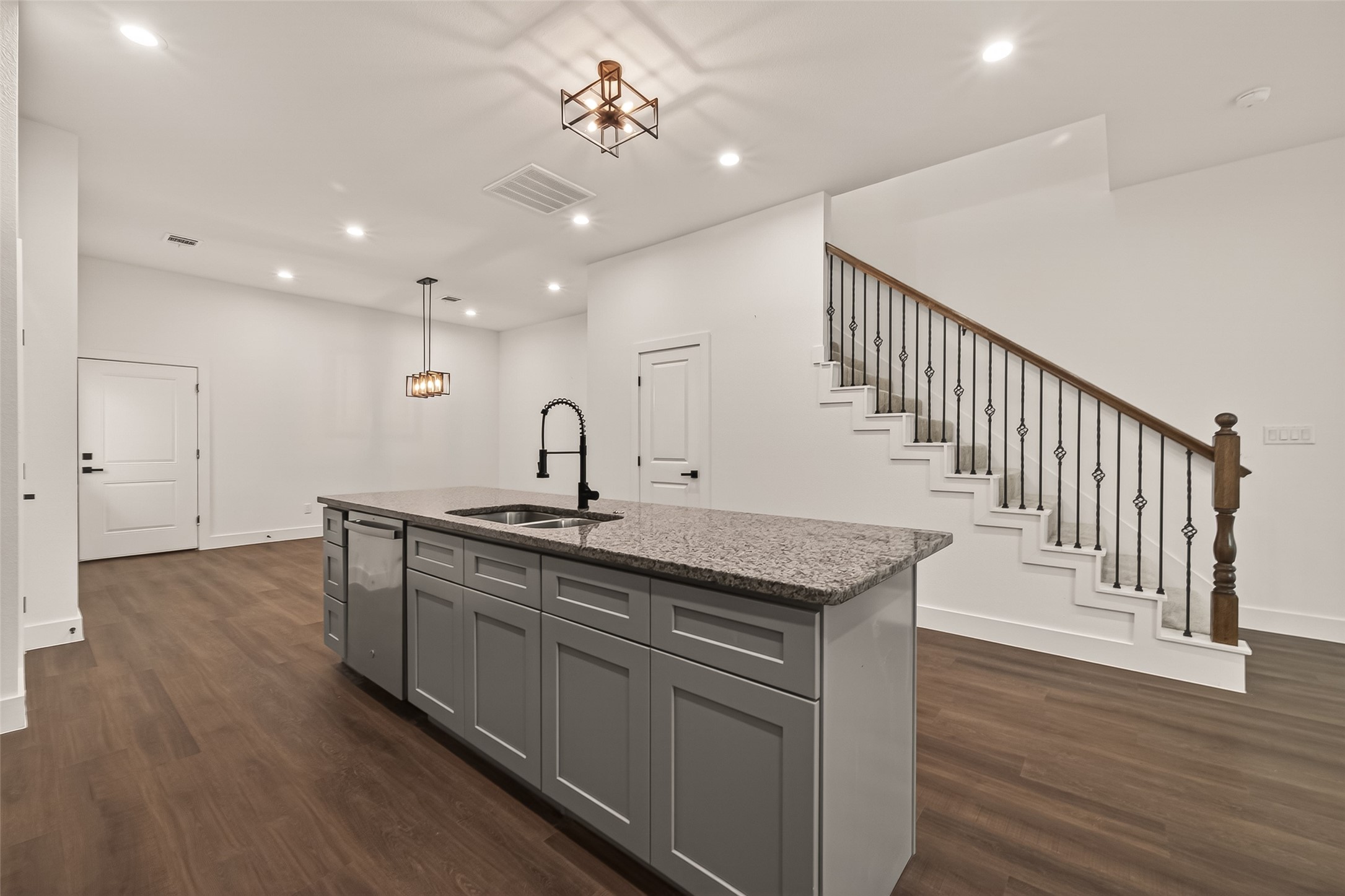 6808 Madrid Street Houston, TX 77021 - Photo 11 of 31 This modern home features an open-concept kitchen with a large island, granite countertops, and sleek cabinetry. It has a stylish staircase with decorative iron railing, recessed lighting, and wood flooring, providing a warm and inviting atmosphere.