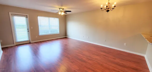 an empty room with wooden floor chandelier fan and windows