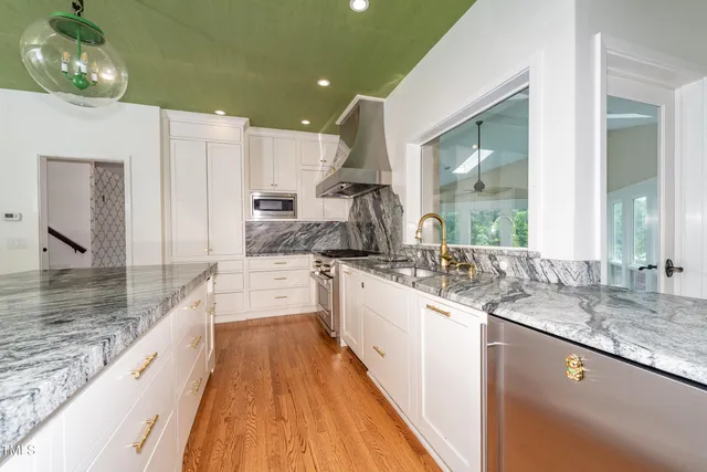 a large white kitchen with kitchen island granite countertop a large counter top space a sink stainless steel appliances and cabinets