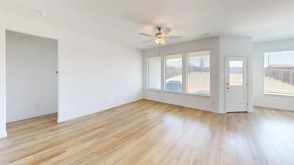 an empty room with wooden floor chandelier fan and windows