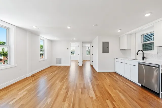 a view of a kitchen with kitchen island wooden floors stainless steel appliances a window and a sink