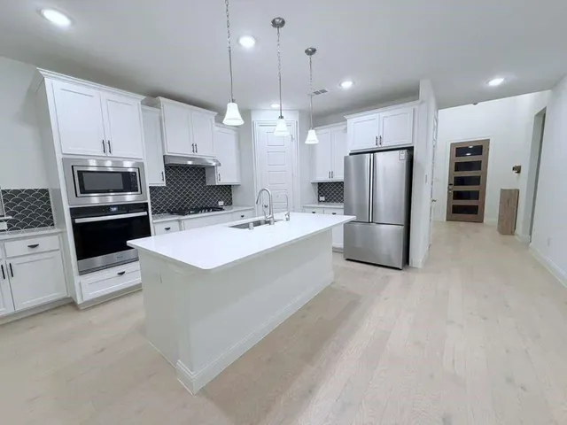 a kitchen with stainless steel appliances a refrigerator a stove a sink a oven and white cabinets with wooden floor