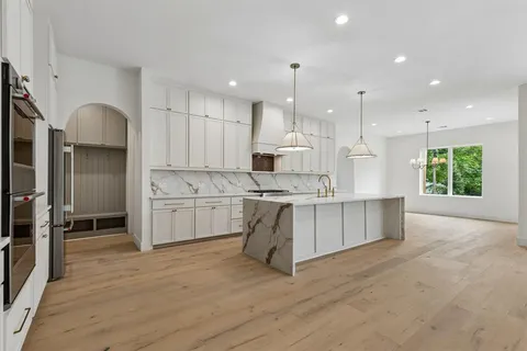 a kitchen with stainless steel appliances kitchen island granite countertop a stove a sink a refrigerator and white cabinets with wooden floor