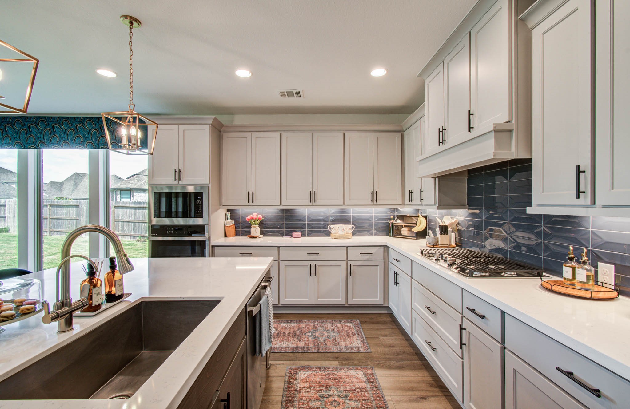 24430 Switchgrass Vly Way Katy, TX 77493 - Photo 14 of 50 This modern kitchen features sleek white cabinetry, a spacious island with a sink, and stainless steel appliances. The room is brightened by large windows and stylish lighting fixtures, creating an inviting and functional space ideal for cooking and entertaining.