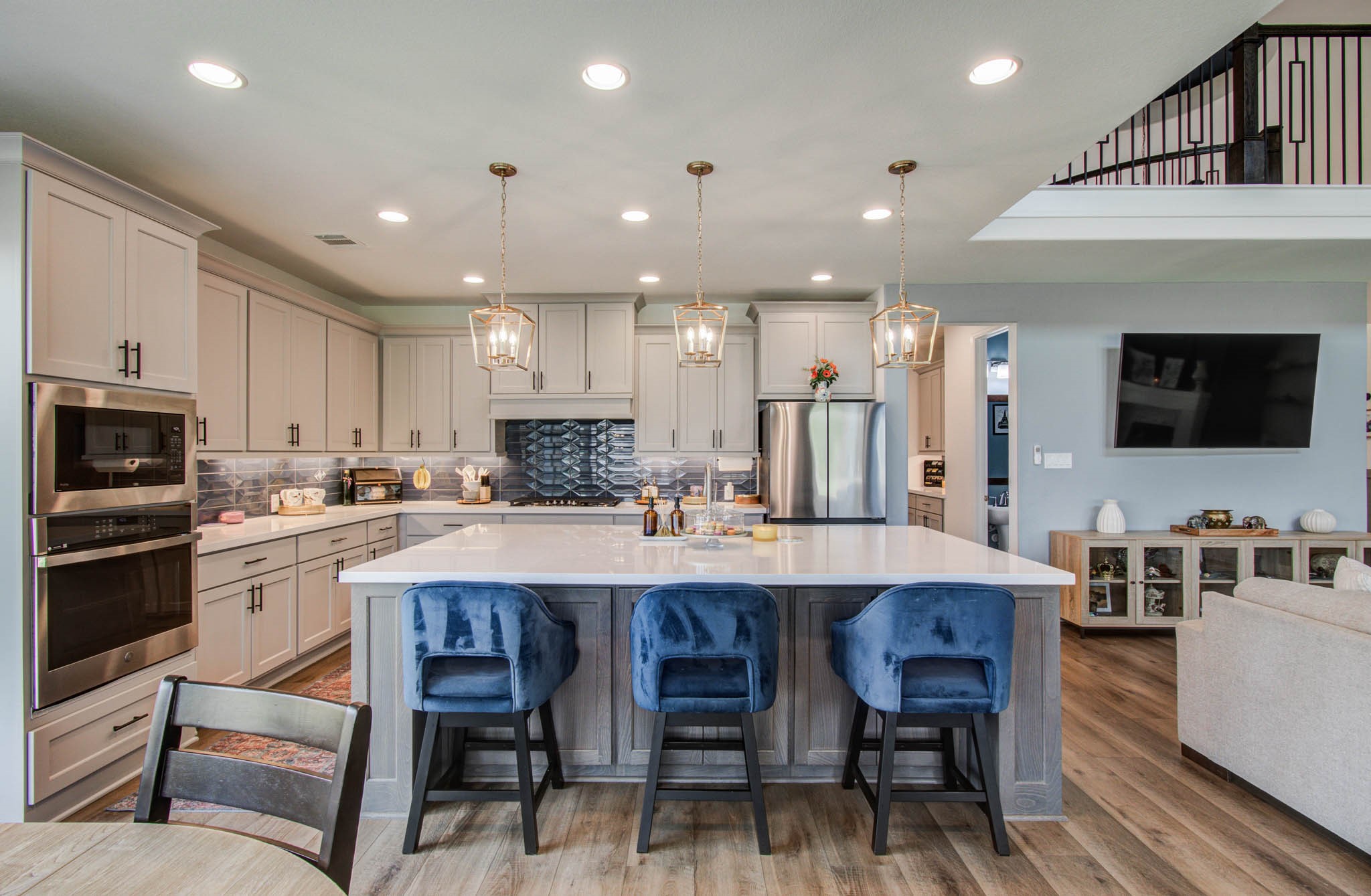 24430 Switchgrass Vly Way Katy, TX 77493 - Photo 16 of 50 This photo showcases a modern, open-concept kitchen with a large island and seating for three. The living area is visible with a wall-mounted TV, creating a seamless flow between spaces.