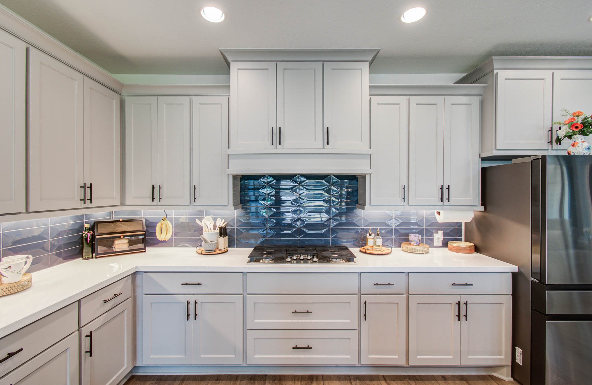 24430 Switchgrass Vly Way Katy, TX 77493 - Photo 18 of 50 This modern kitchen features sleek white cabinetry, a striking blue geometric tile backsplash, and stainless steel appliances. The space is well-lit with recessed lighting and offers ample counter space for cooking and entertaining.