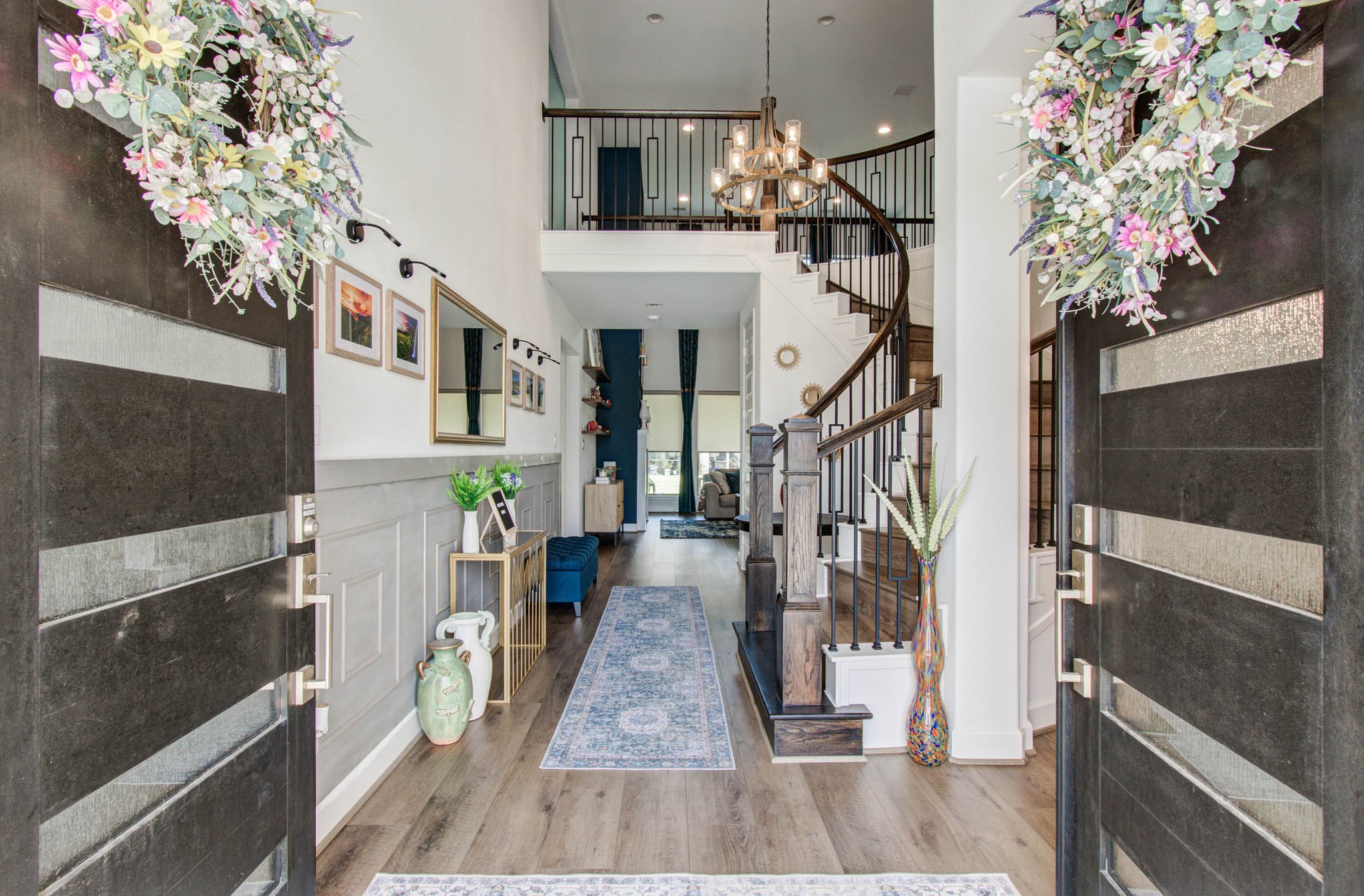 24430 Switchgrass Vly Way Katy, TX 77493 - Photo 4 of 50 Welcome to a stunning home with a grand entrance featuring double doors adorned with floral wreaths. Inside, a bright, open foyer with elegant wood flooring leads to a graceful curved staircase. The space is accented with stylish light fixtures, and decorative elements, creating an inviting and sophisticated ambiance.